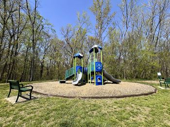 A playground with a blue and green slide and two green benches.